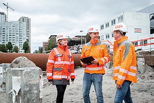 Zwei Bauarbeiter mit Helm betrachten ein aufgestelltes Messgerät