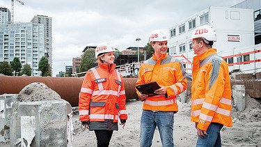 Zwei Bauarbeiter mit Helm betrachten ein aufgestelltes Messgerät